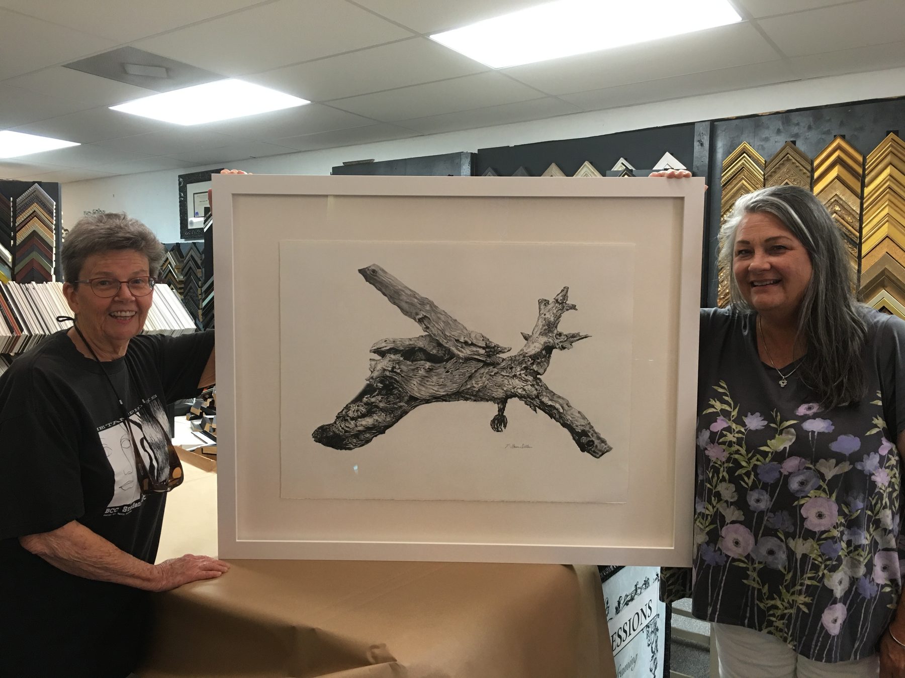 Customers with a freshly framed piece, with the frame sample wall behind
