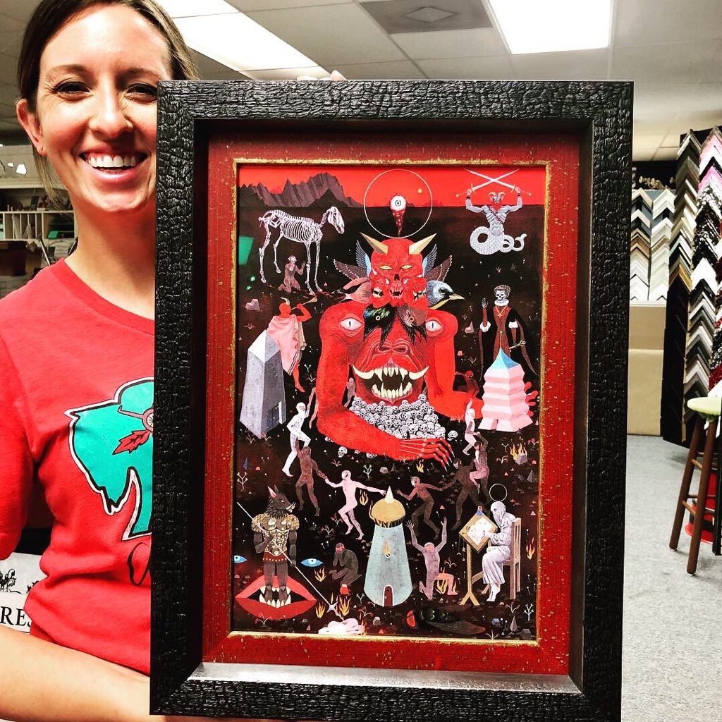 Framed folk art piece in a black frame, at the sample wall